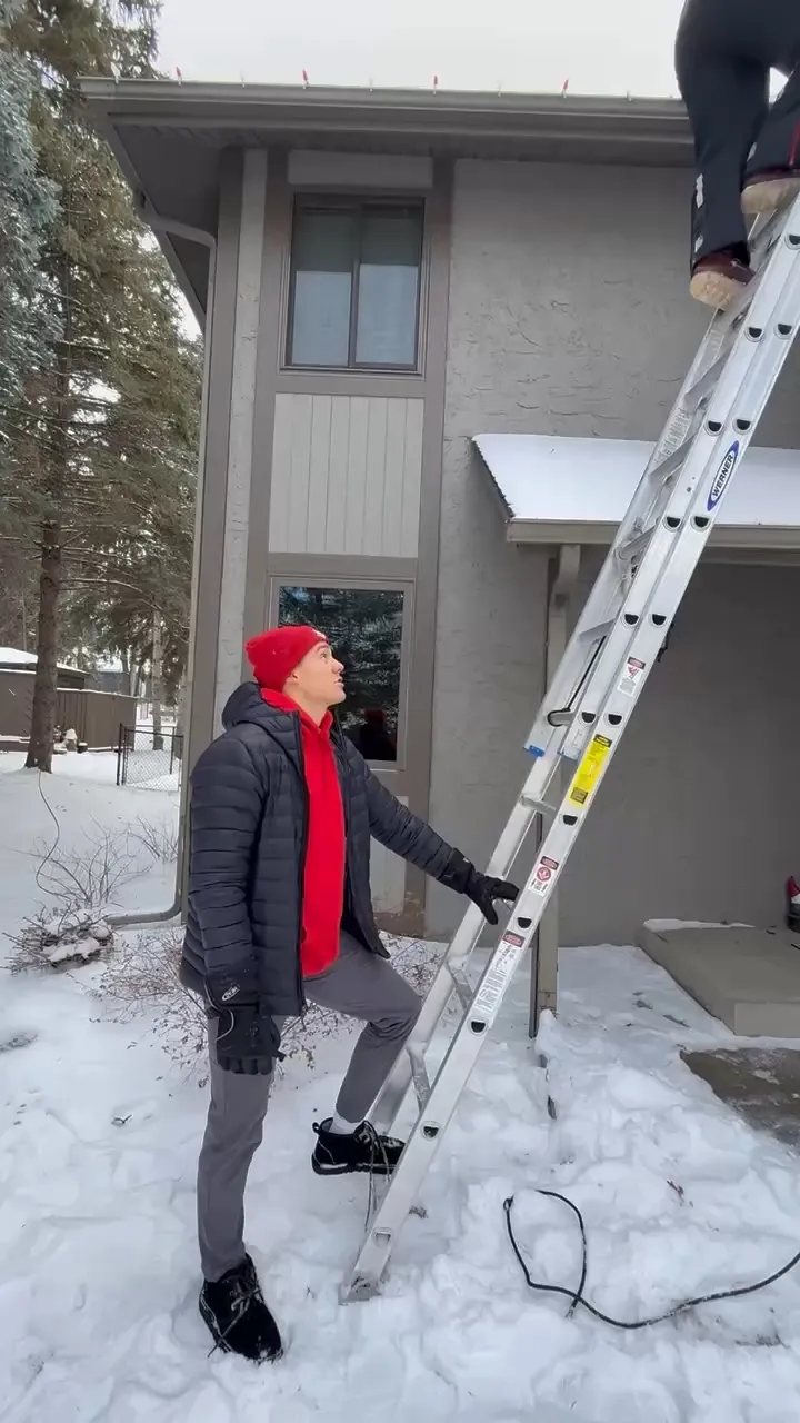 Crew member in a red beanie on a ladder in the snow